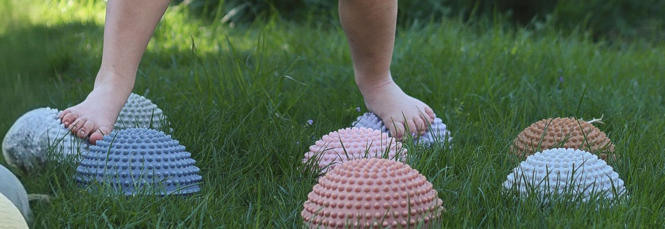 barn med bare fødder går på sansesten i pastelfarver med knopper, perfekt legetøj til sansestimulation i børnehave fås hos Nordic Simply