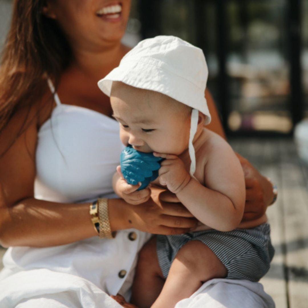 Baby sidder på mor og bider i blå badedyr formet som en påfugl i naturgummi fra Natruba fås hos Nordic Simply