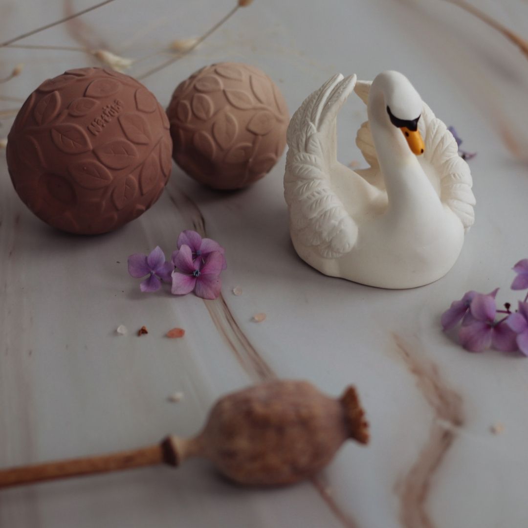 Hvid svane badedyr i naturgummi fra Natruba, set på marmor baggrund sammen med to brune sansebolde