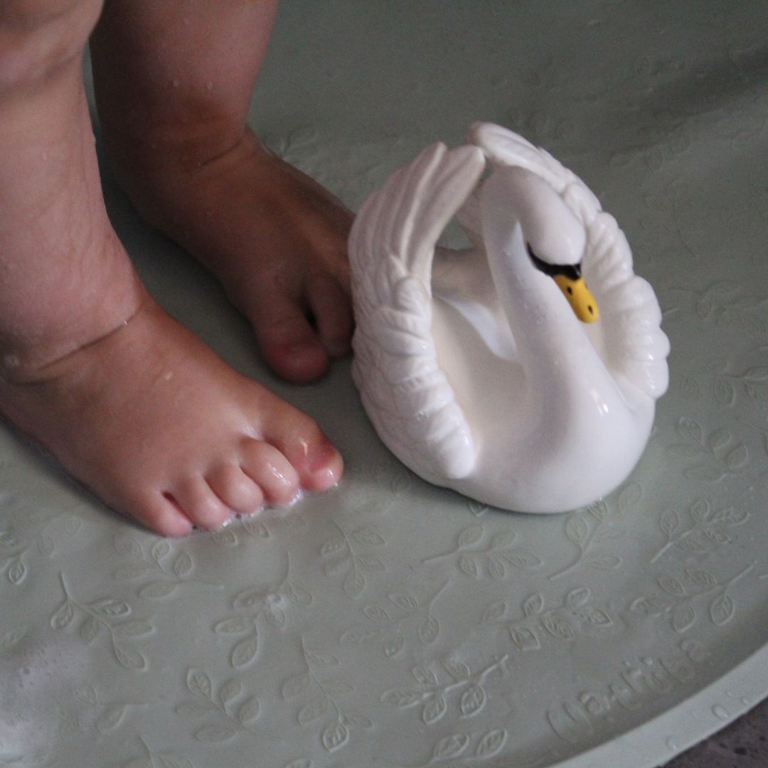 Hvid svane badedyr i naturgummi fra Natruba, set på bademåtte foran fødder i bad