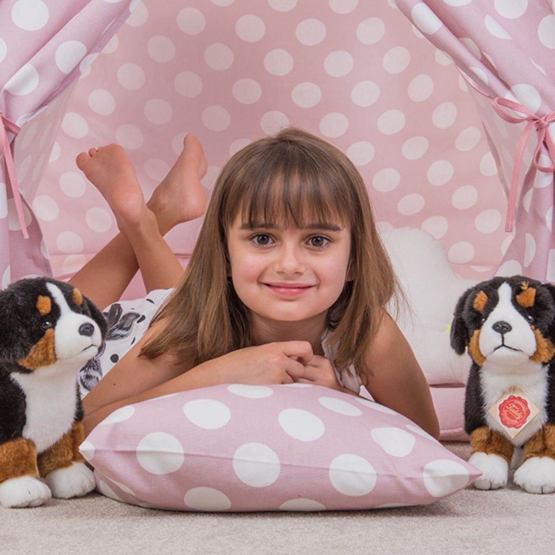 Pige i rosa telt med hvide polkaprikker ligger på maven med 2 Berner Sennen bamser, rundt om sig, ligner ægte hundehvalpe, fra Teddy Hermann