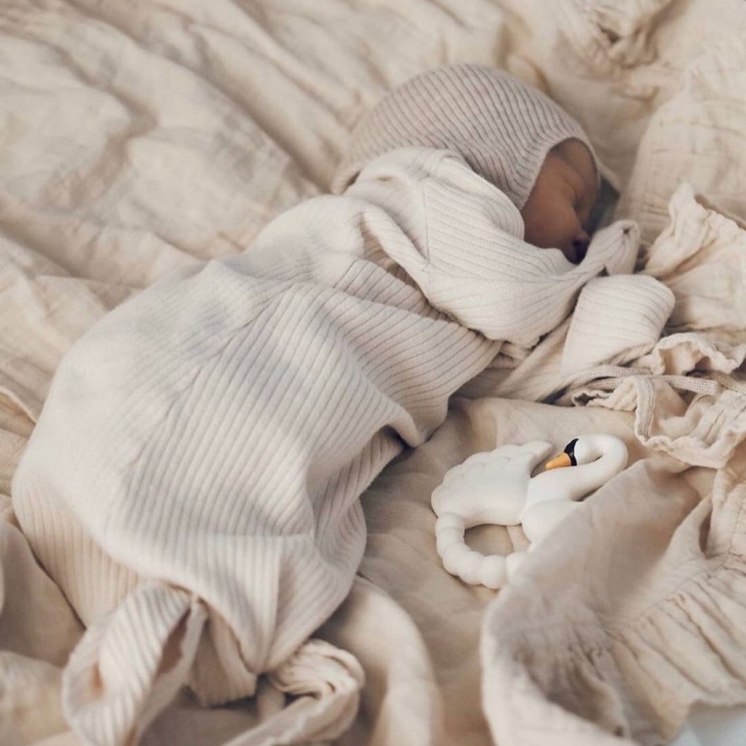 Nyfødt baby ligger og sover ved siden af hvid bidering formet som en svane i naturgummi fra Natruba.
