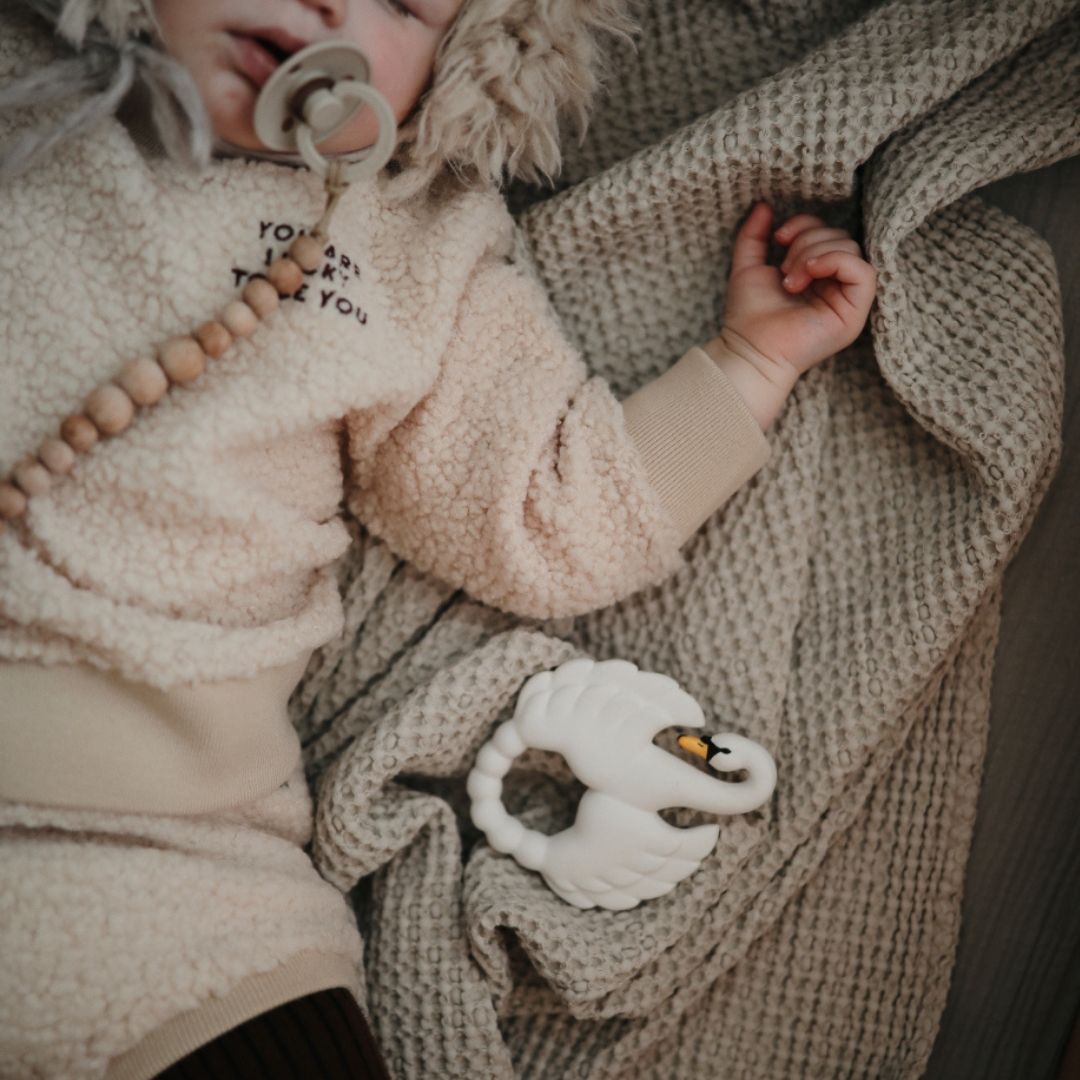 Hvid bidering formet som en svane i naturgummi fra Natruba, ligger ved siden af baby der sover, fås hos Nordic Simply