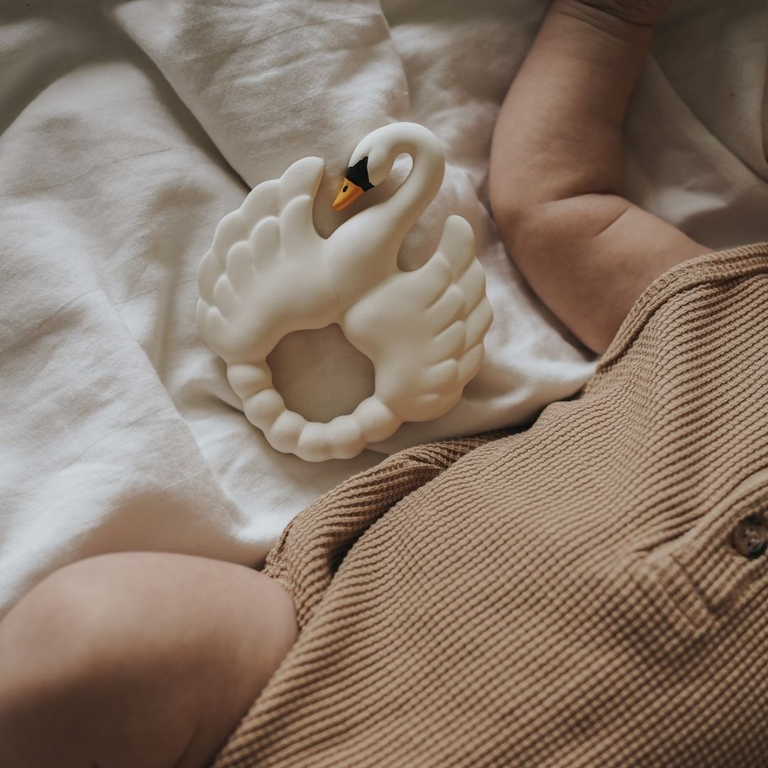 Hvid bidering formet som en svane i naturgummi fra Natruba, ligger ved siden af baby i seng, fås hos Nordic Simply