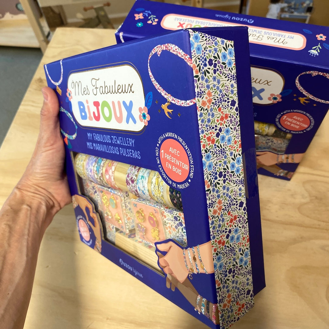 Hånd holder smykkesæt fra Auzou til børn i stor blå æske: Lav smukke stof-armbånd med vedhæng, fås hos Nordic Simply