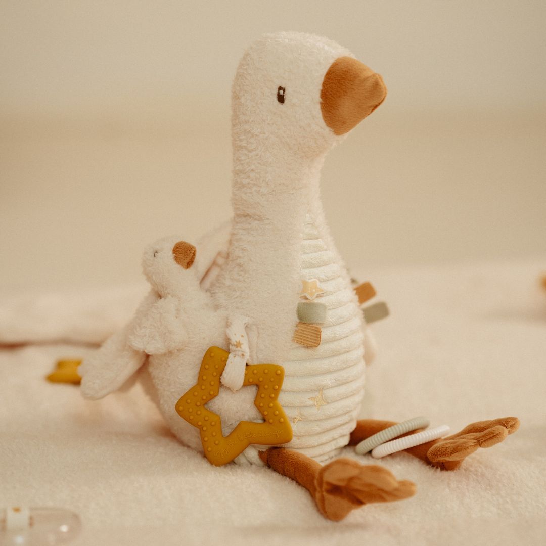 Beige aktivitetsbamse fra Little Dutch, formet som en gås med sjove ting at opdage for baby, blandt andet en gul stjernebidering, her set på lyst tæppe med lys baggrund, fås hos Nordic Simply