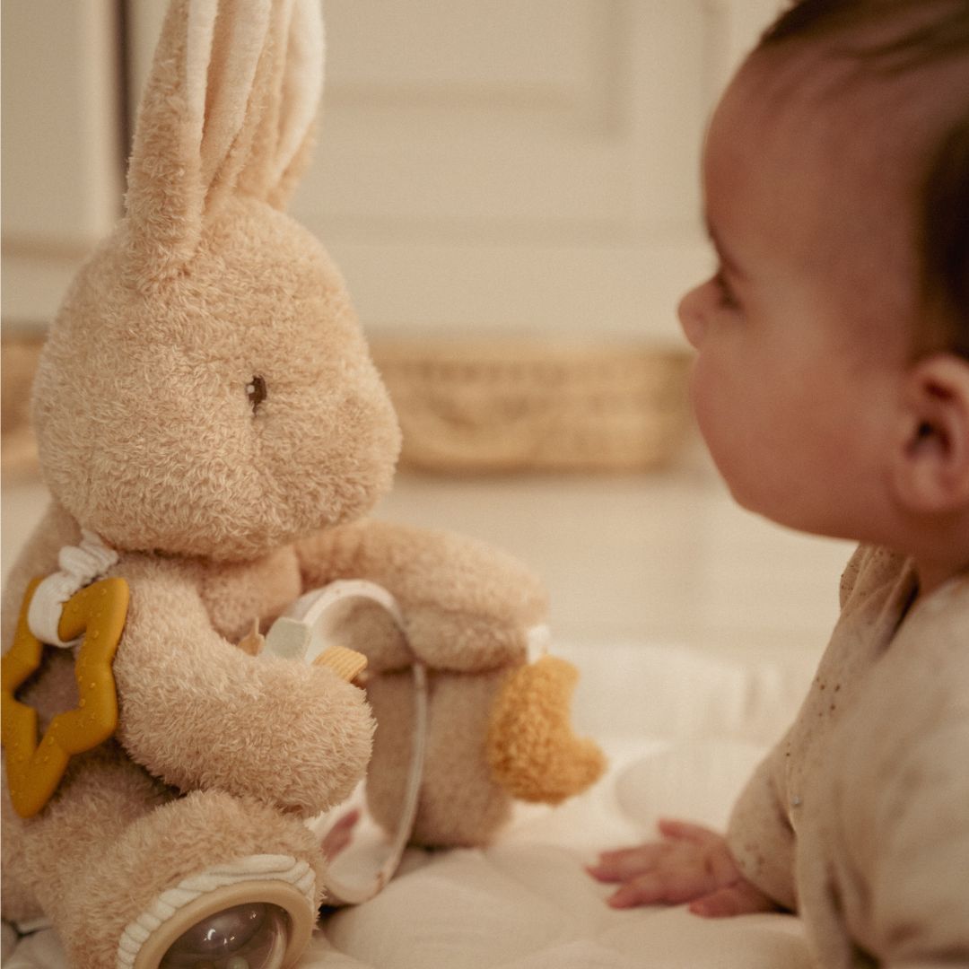 Baby i lyst værelse ser på beige kanin aktivitetsbamse fra Little Dutch, fås hos Nordic Simply