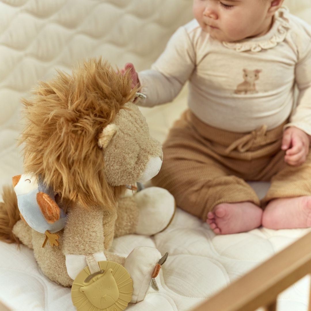 Baby sidder på lyst tæppe og rører ved løve aktivitetsbamse. En sød bamse med masser at udforske fra nyfødt og op. Little Dutch.