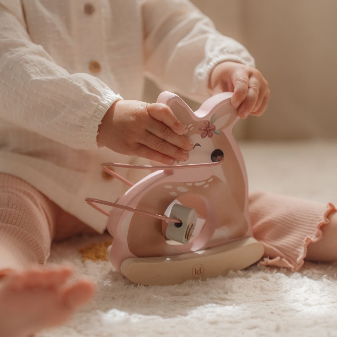 Barn på lyst legetæppe med rådyr aktivitetsdyr rosa i træ med sjove perler til leg og motorik.