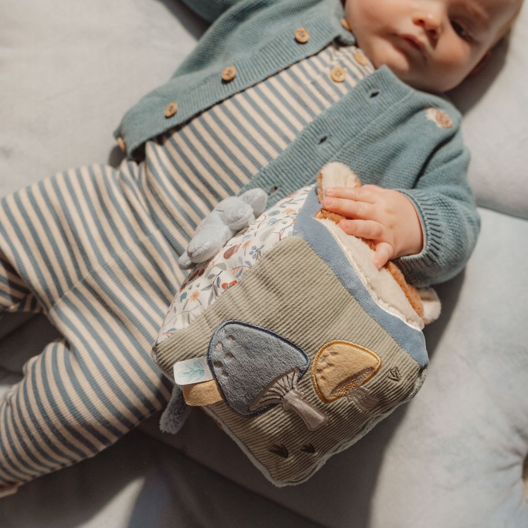 Baby ligger og holder blå aktivitetsterning med dyremotiver.