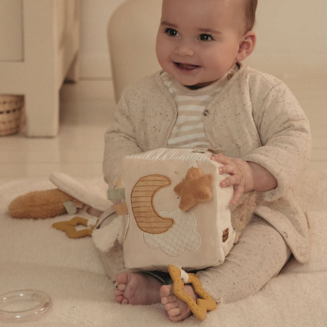 smilende baby i lyst tøj i lyst værelse med beige aktivitetsterning i stof med måne og aktiviteter, fra Little Dutch, fås hos Nordic Simply