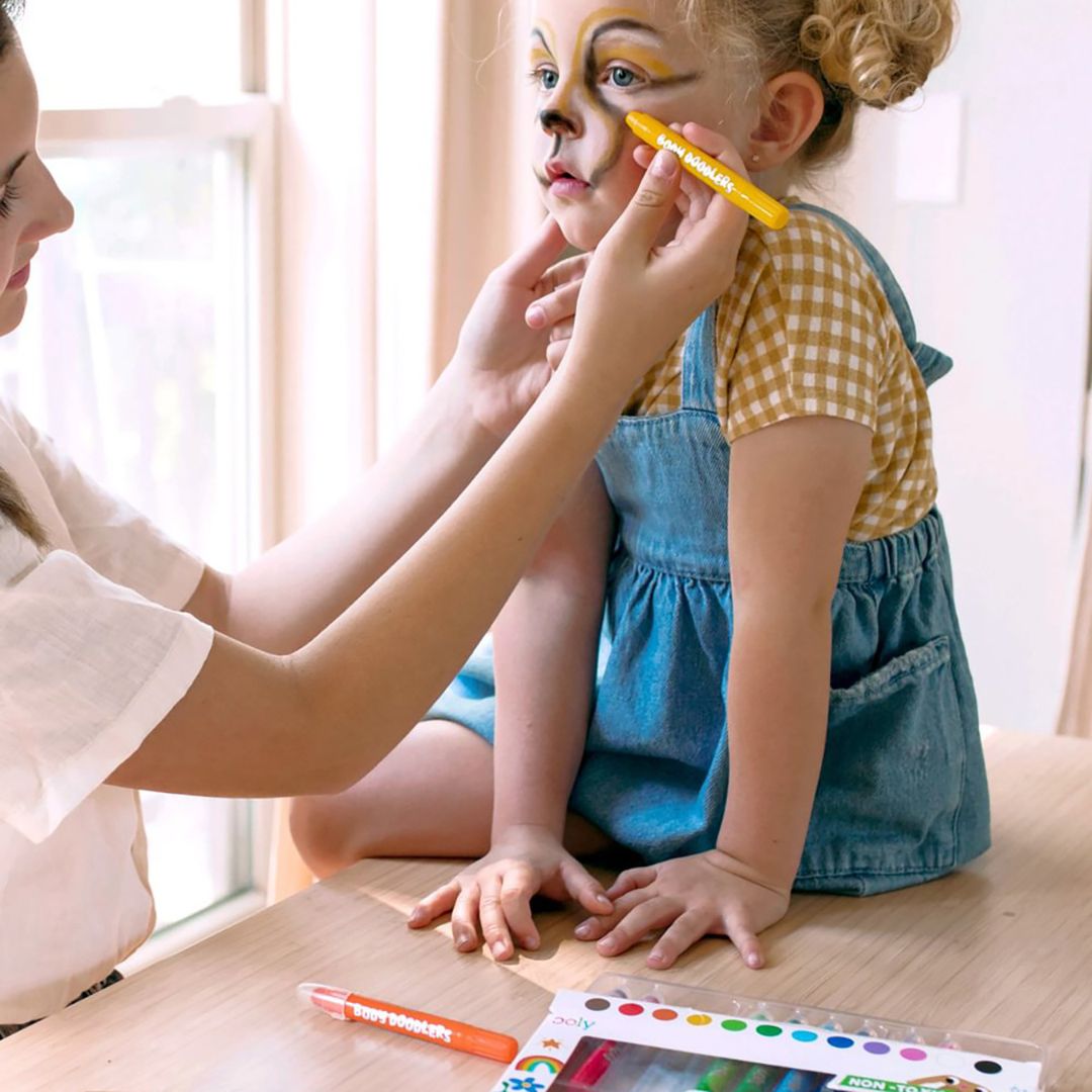Barn bliver dekoreret med OOLY ansigts- og kropsmaling på kinderne, let at bruge og vaske ud.