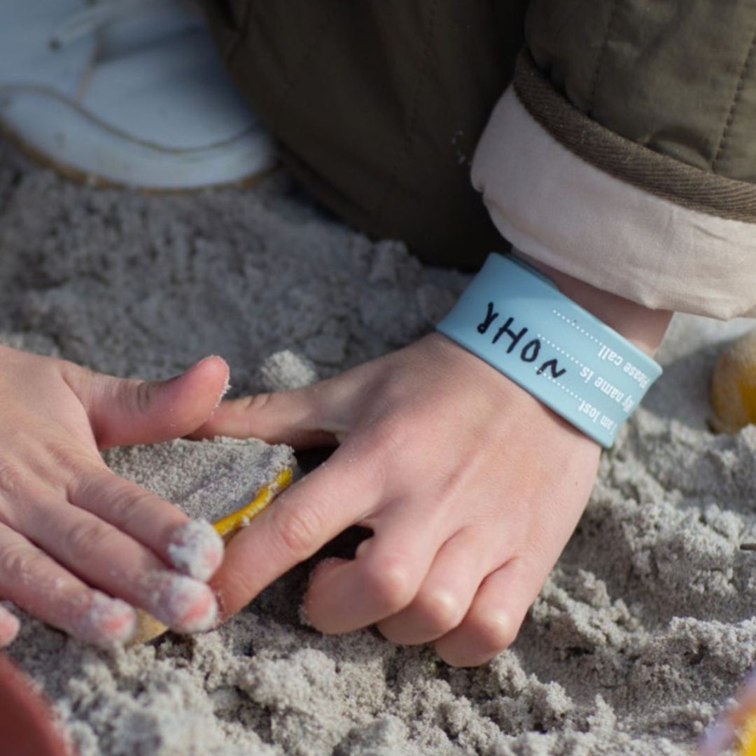 Hånd med lyseblå armbånd "jeg er blevet væk" med felter til at skrive barnets navn og dit telefonnummer, fra Scrunch fås hos Nordic Simply