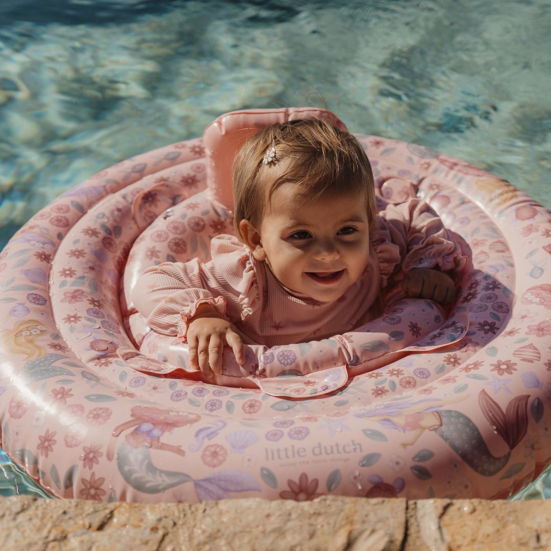barn i pool i rosa babybadering med havfruer og motiver af havets dyr. Perfekt babyflyder med fire kamre, rygstøtte og håndtag. Egnet fra 6-12 mdr.