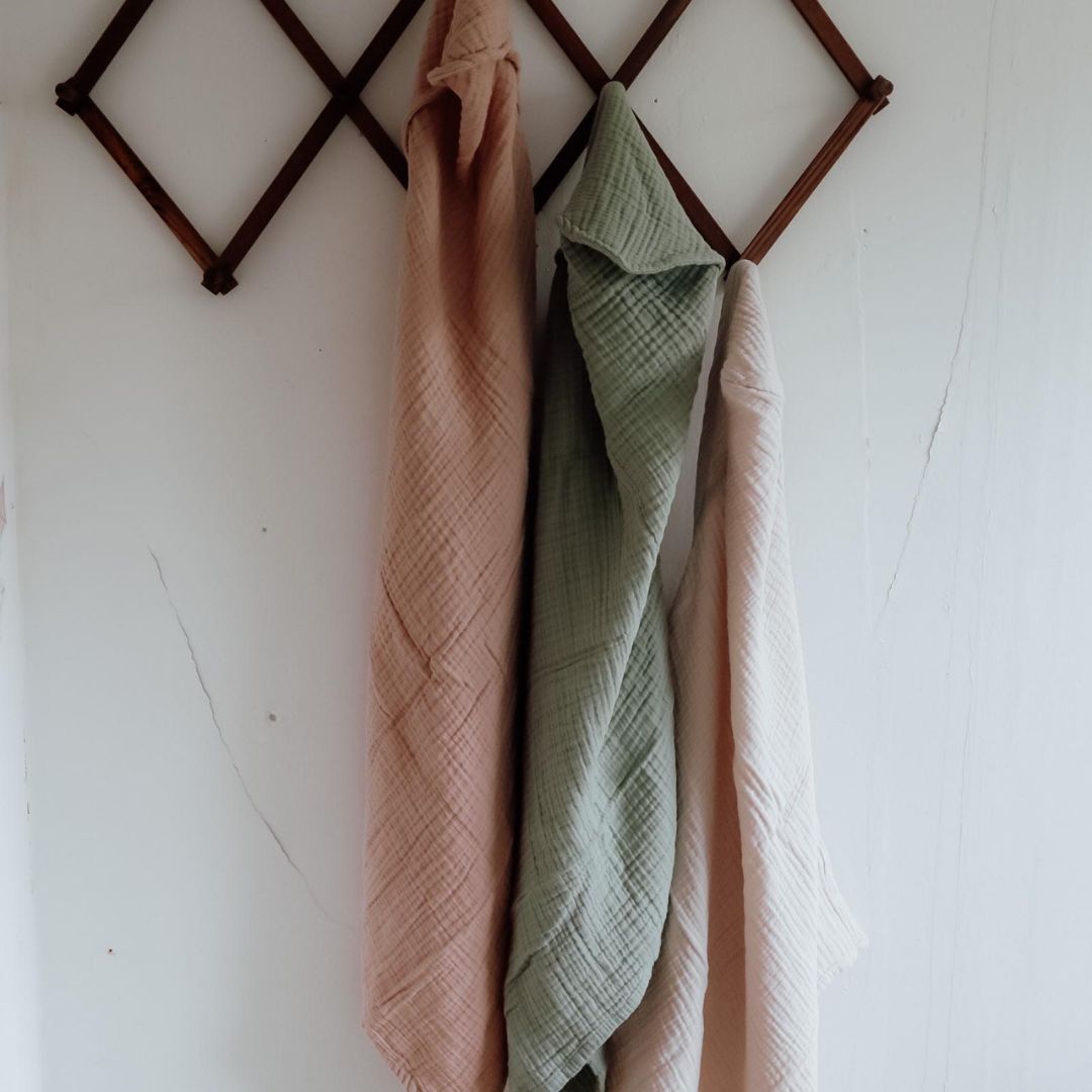 To badehåndklæde i rosa og grøn til baby med hætte i 100% økologisk rosa bomuld muslin fra Natruba, hænger på gammel knagerække i træ.