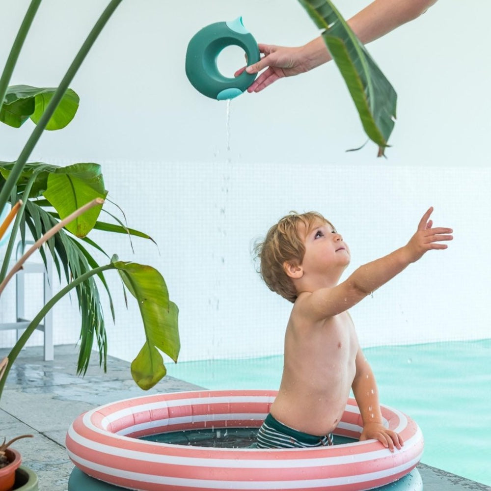 dreng sidder i lille rundt badebassin med to ringe, en grøn og en orange med hvide striber, bassinet har en diameter på 80 centimeter og er derfor til små børn under opsyn.