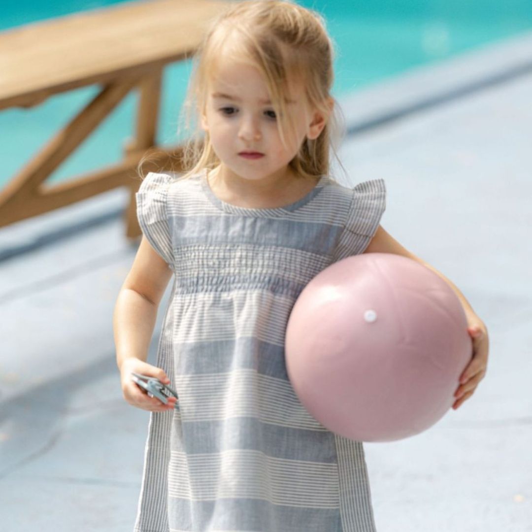 Pige ved pool holder lille rosa badebold i silikone med ru overflade, god at gribe og let at puste op fra Scrunch