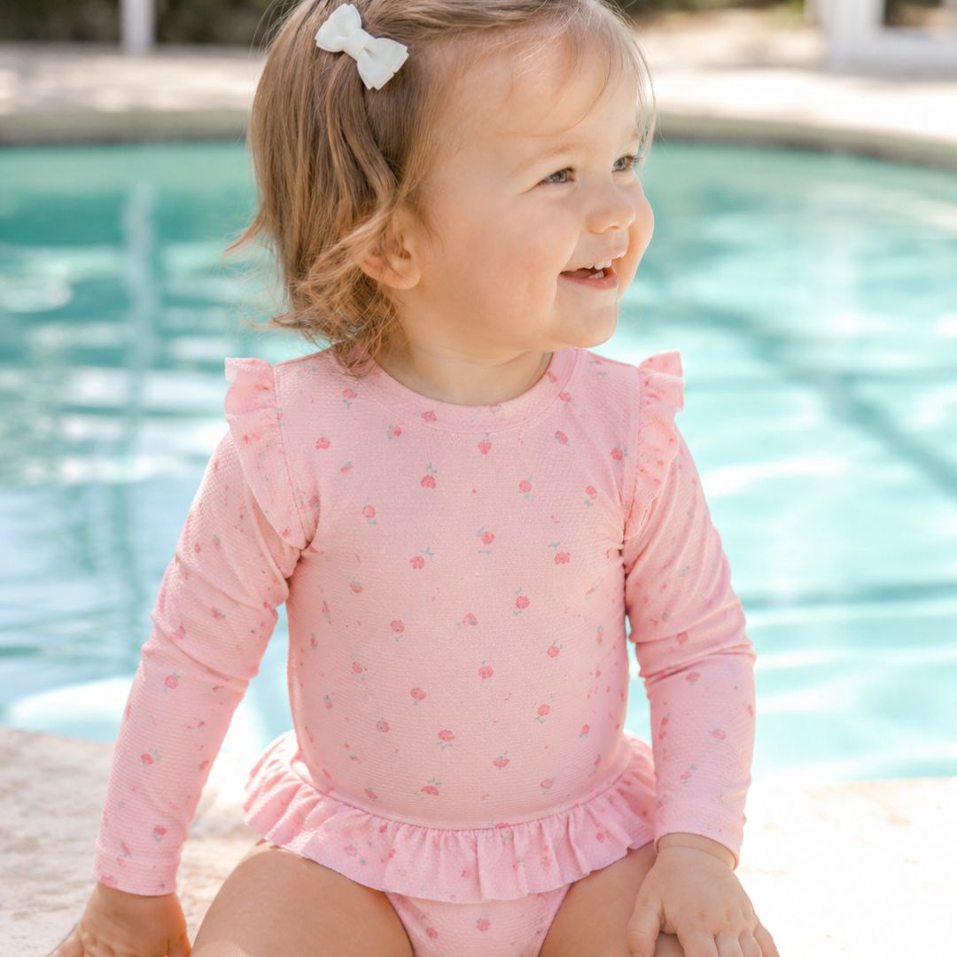 pige ved pool i pink badedragt med lange ærmer og pink motiver af blomster, badedragt med UV40 beskyttelse.