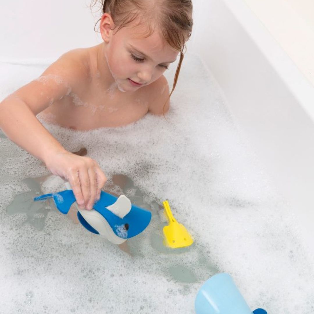 Pige leger i bad med blå badehvaler af skum, badelegetøj til børn fra 3 år og op, fra Quut fås hos Nordic Simply