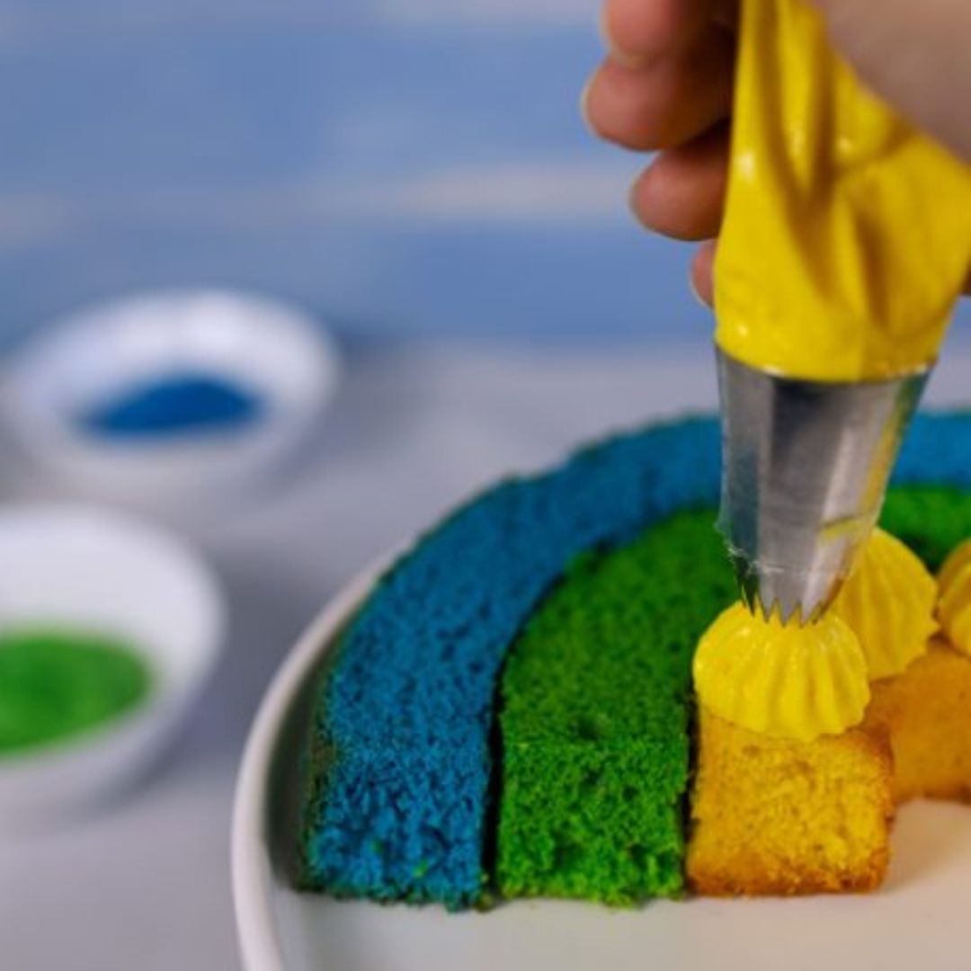 Regnbuekage i tre farver blå, grøn og gul, sprøjtes med gul creme, bagt i grøn regnbue bageform i silikone fra Dëna fås hos Nordic Simply