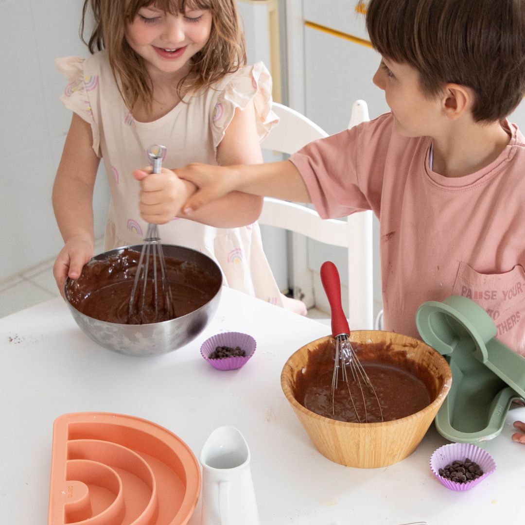 To børn i lyst køkken rører chokoladekage-dej, som skal i rosa regnbue bageform fra Dëna fås hos Nordic Simply