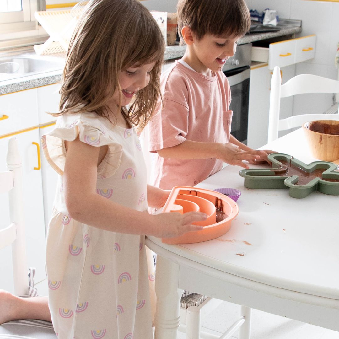 To børn i lyst køkken bager med bageforme fra Dëna, en af dem rosa regnbue bageform