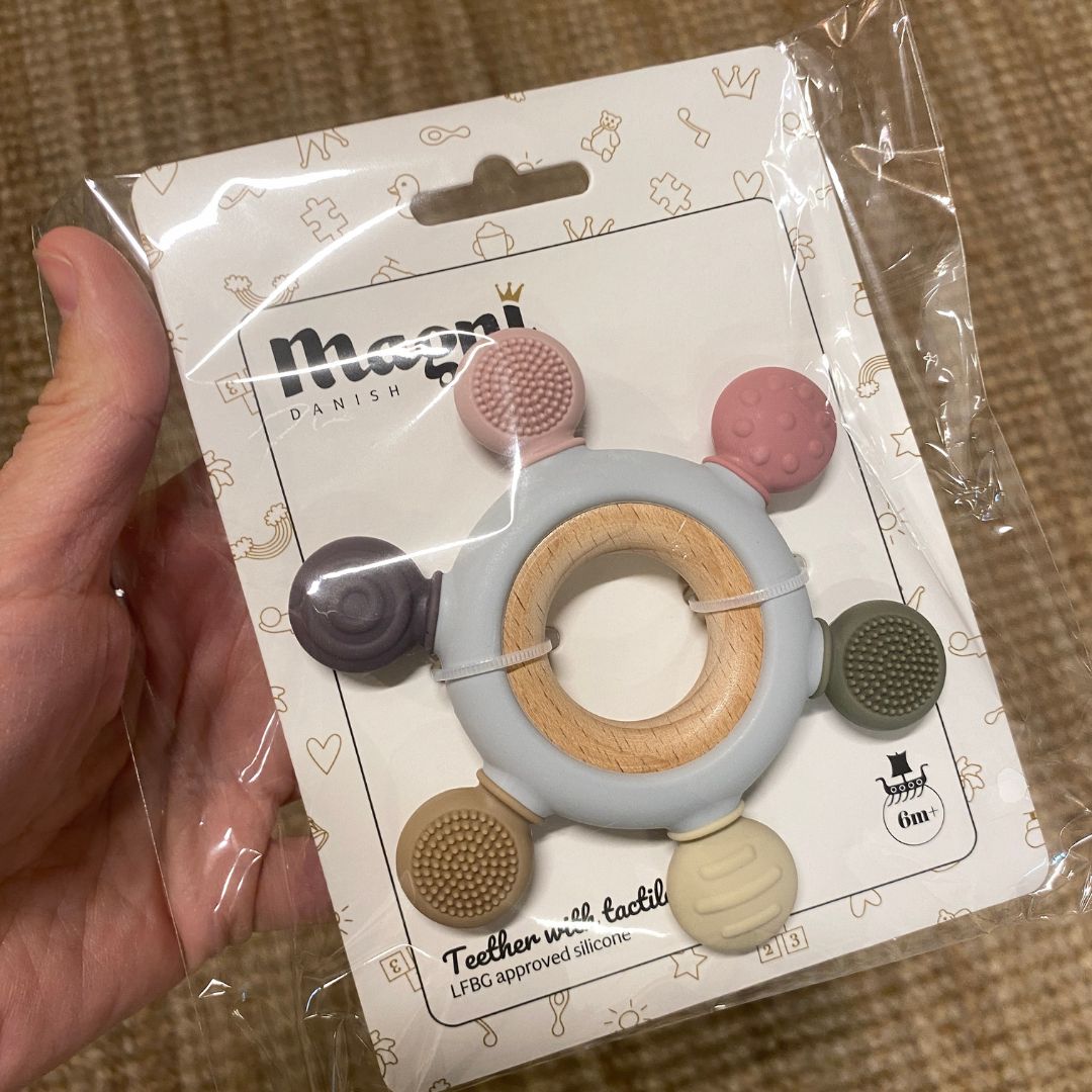 Hånd holder multifarvet bidering i silikone på træring fra Magni hos Nordic Simply