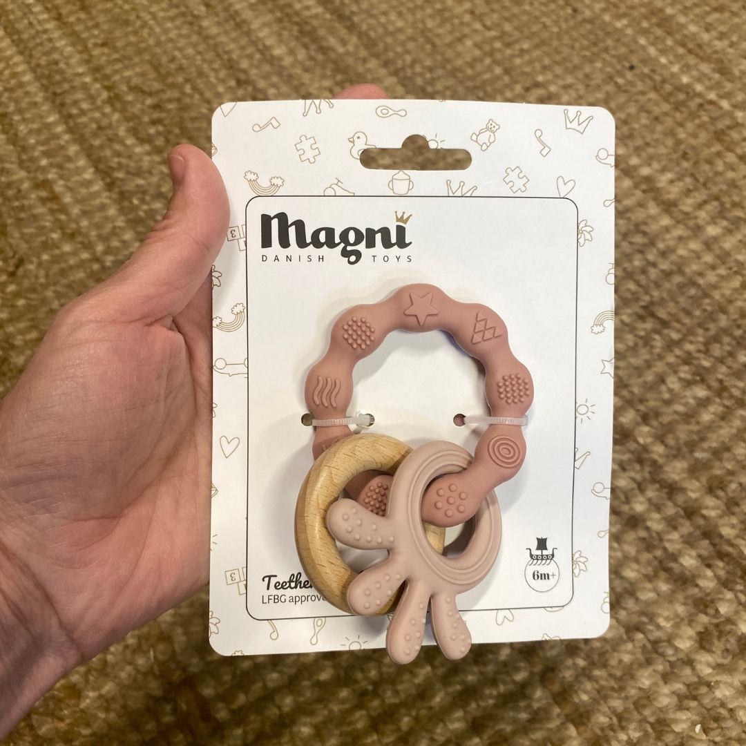 Hånd holder pakke med rosa biderangle i silikone med træring fra Magni hos Nordic Simply