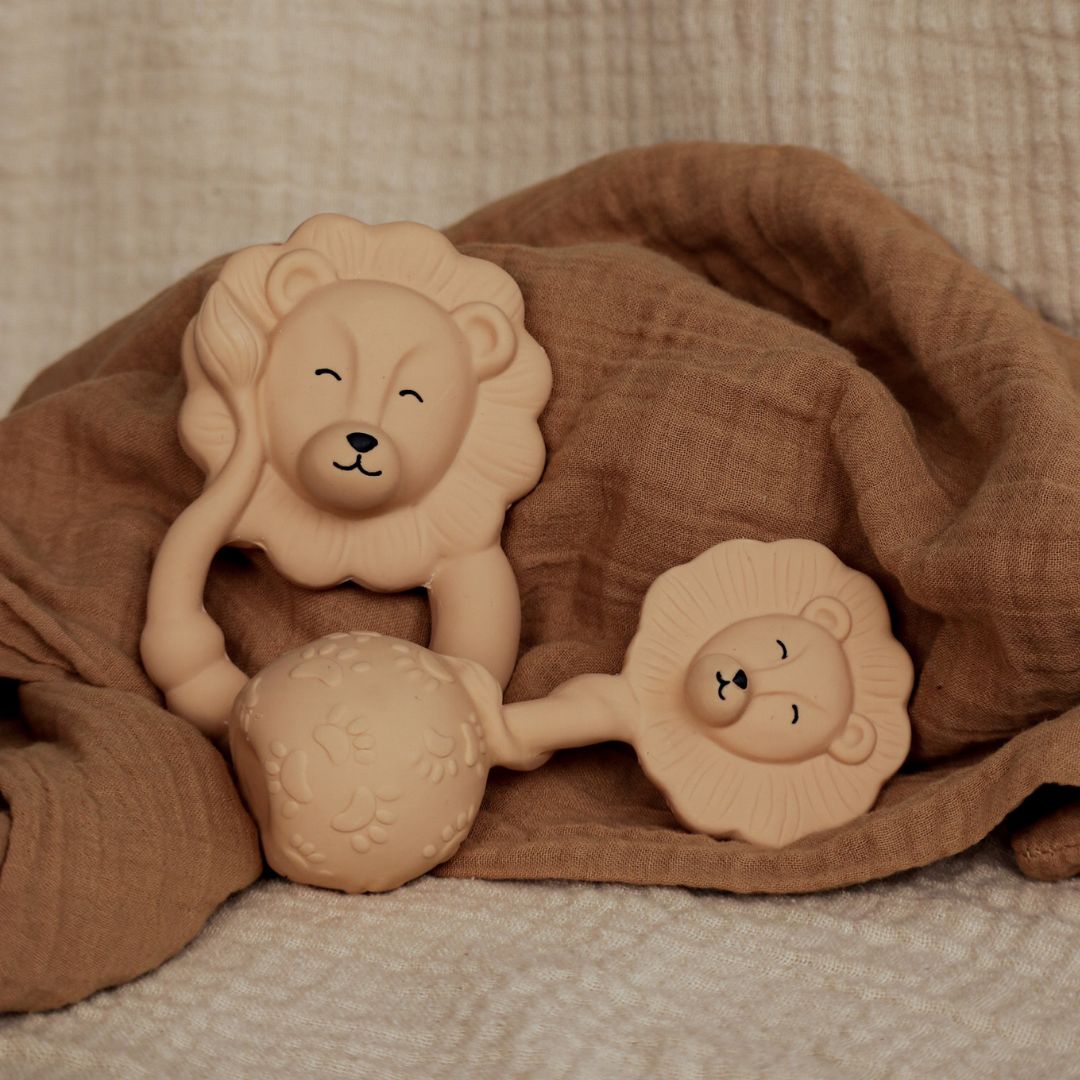 Beige bidering og rangle formet som løver i naturgummi fra Natruba, set på baggrund af brunt svøb, fås hos Nordic Simply