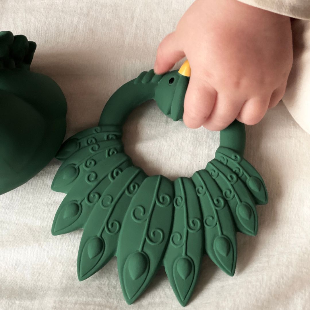 Babyhånd holder grøn bidering formet som en påfugl i naturgummi fra Natruba fås hos Nordic Simply