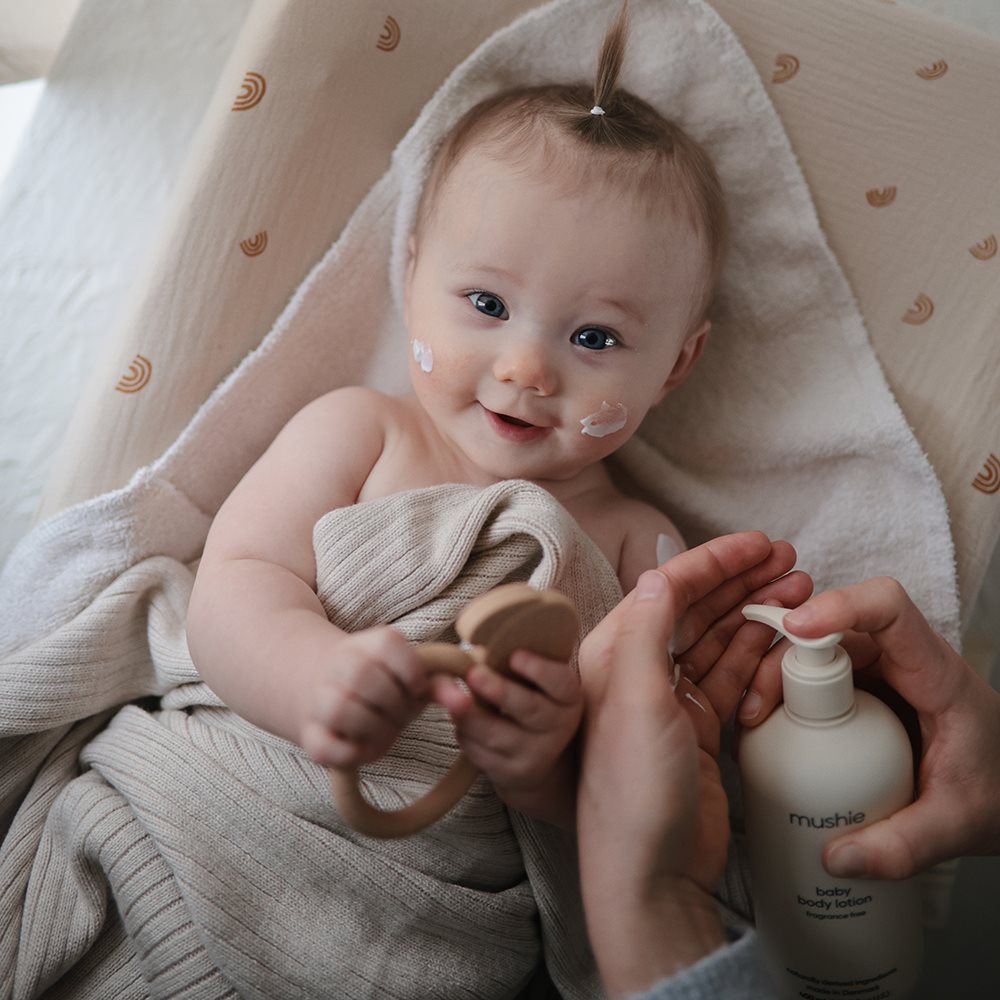 Baby med Mushie bodylotion på kinderne. Parfumefri, Svanemærket babylotion, produceret i Danmark.