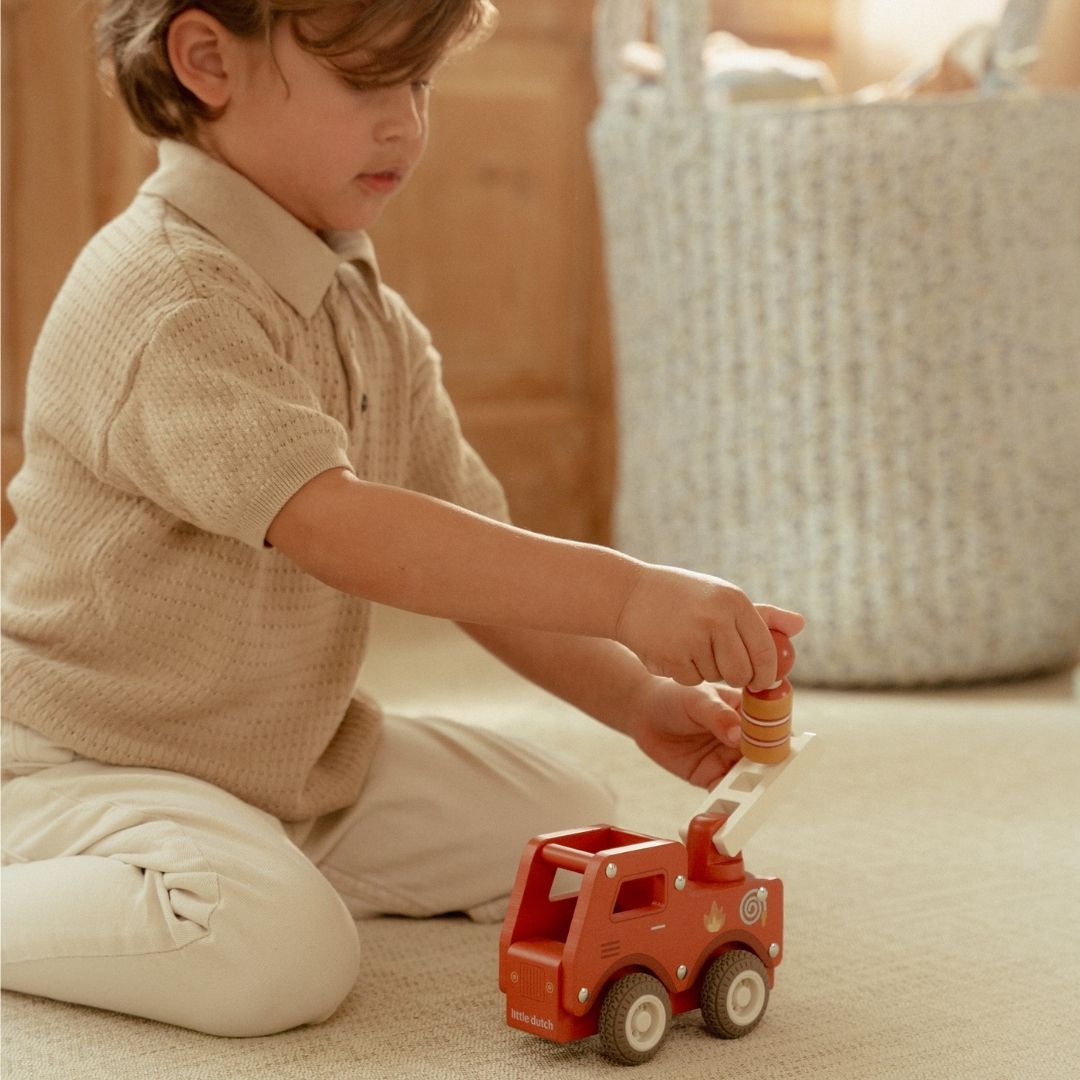 Brandbil med træfigur: en dreng leger med en rød træbrandbil og bruger stigen til redning.