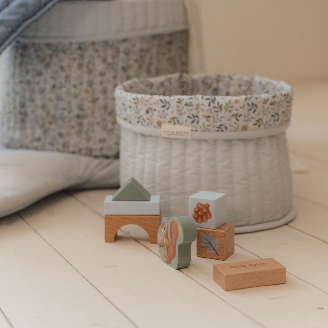 Træklodser i blå nuancer ved siden af en flettet opbevaringskurv, perfekt til leg.