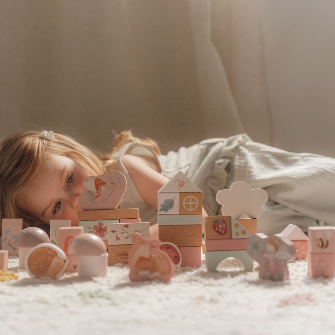 Barn leger med rosa træklodser med feer og dyr fra Little Dutch i et hyggeligt rum.