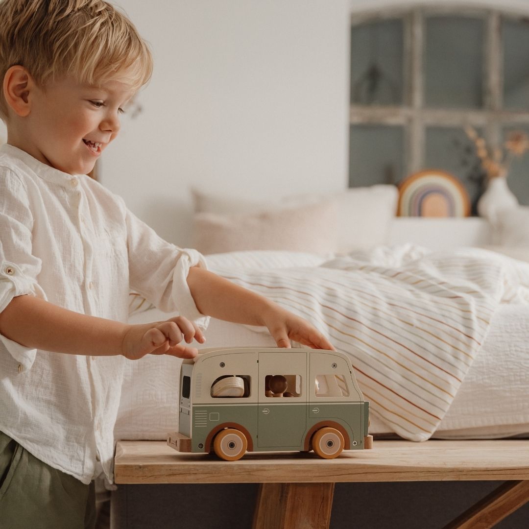 Dreng ler og skubber retrobus i træ i grøn og hvid, fra Little Dutch hen over bord, i lyst soveværelse fås hos Nordic Simply