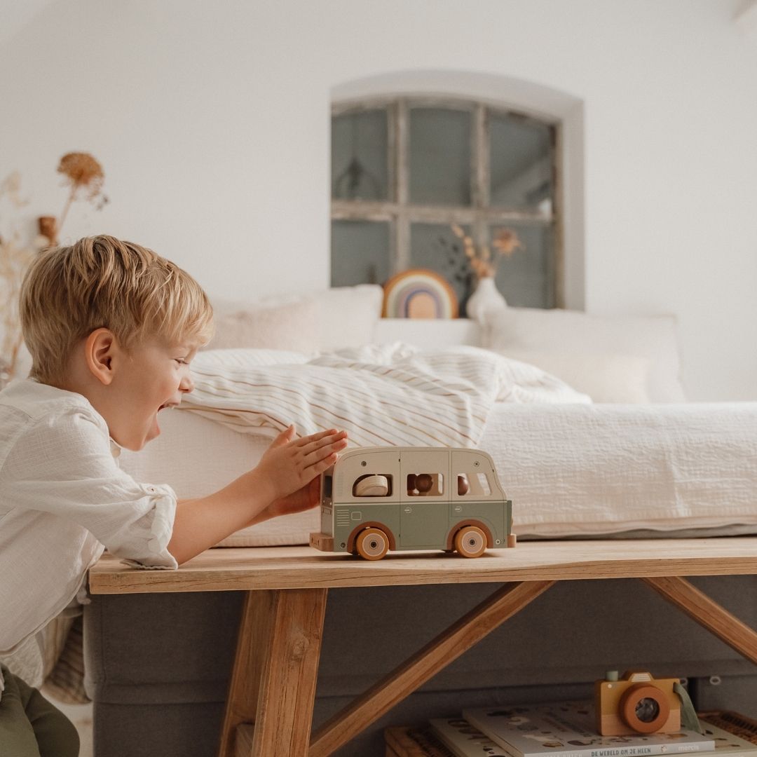Dreng ler og skubber retrobus i træ i grøn og hvid, fra Little Dutch hen over bord i lyst soveværelse.