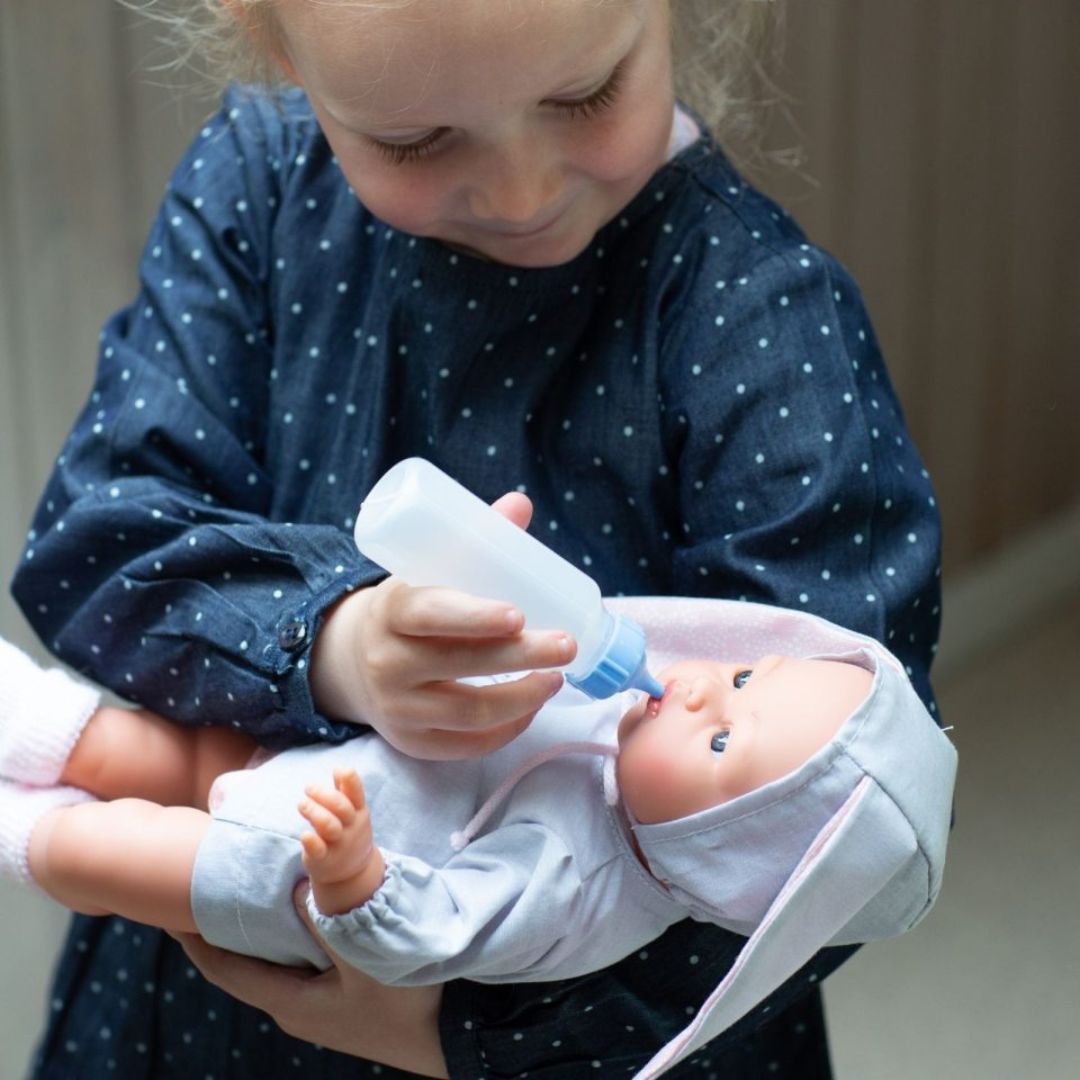 Pige holder dukke, i grå dragt med kaninører, imens hun giver den sutteflaske. Kvalitetsdukke fra spanske Así fås hos Nordic Simply