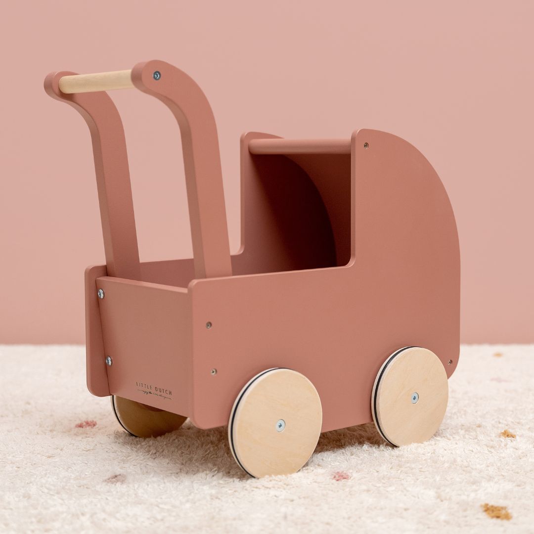 Rosa dukkevogn i træ fra Little Dutch set i værelse med lyst gulvtæppe og rosa væg, fås hos Nordic Simply