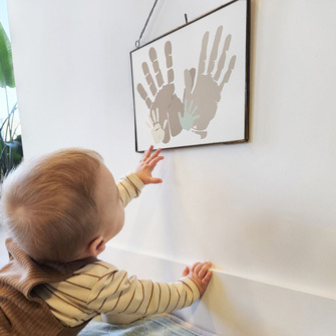 Baby kigger på 4 håndaftryk af familien, som hænger på væggen i sort ramme.