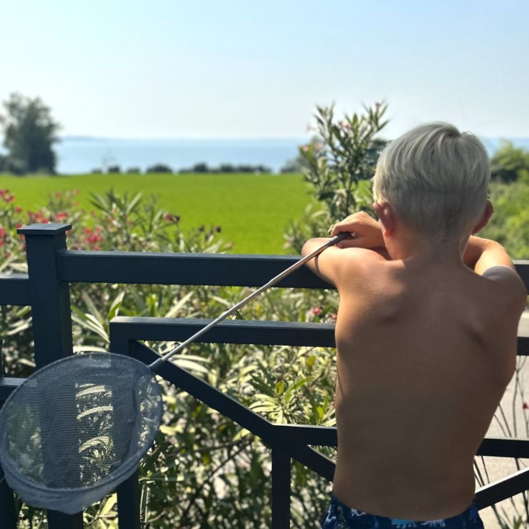 Dreng med ryggen til holder lyseblå fiskenet på teleskopstang