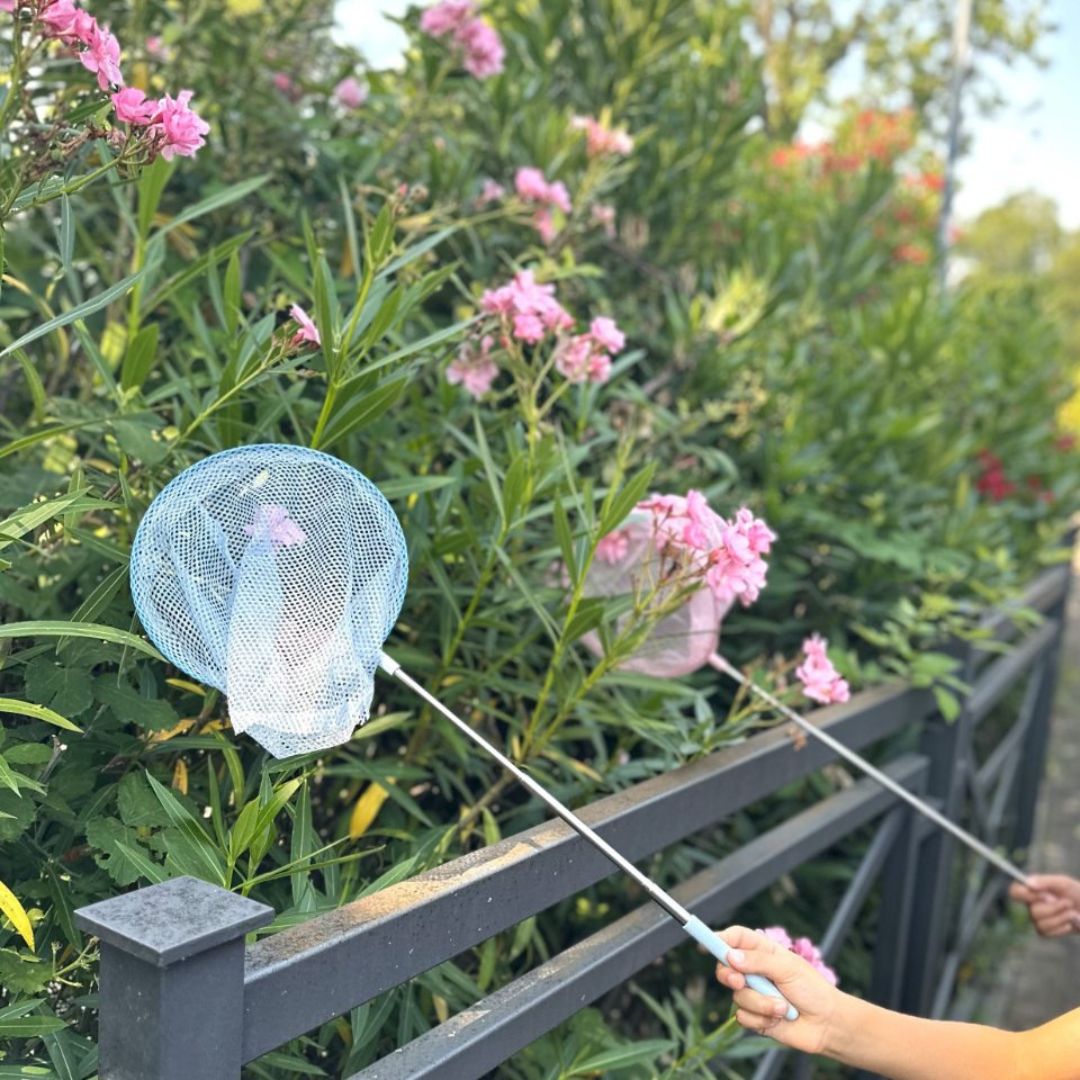 Hænder holder blå fiskenet på teleskopstand i naturen ved grøn busk