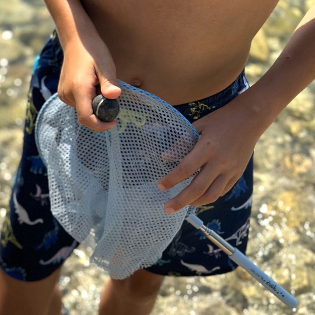 Barn med blå fiskenet på teleskopstang med stenstrand i baggrunden.
