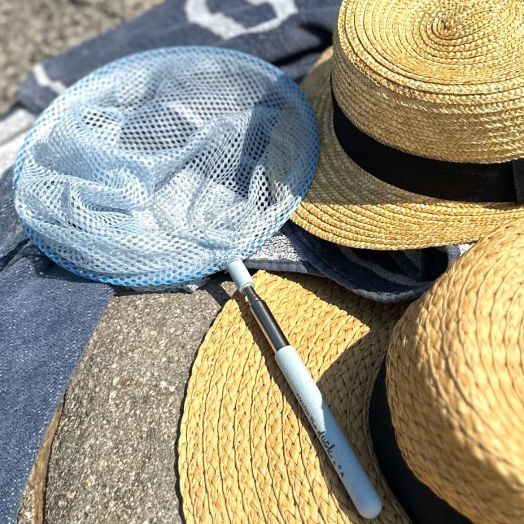 Blå fiskenet på teleskopstang ligger på strandhåndklæde ved siden af to solhatte.