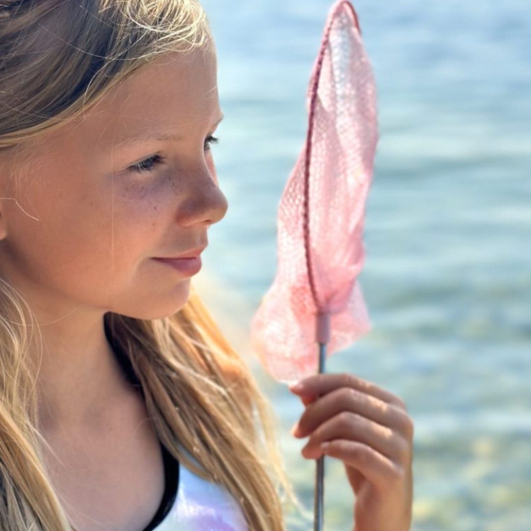 Pige ved strand holder rosa fiskenet på teleskopstang, fås hos Nordic Simply
