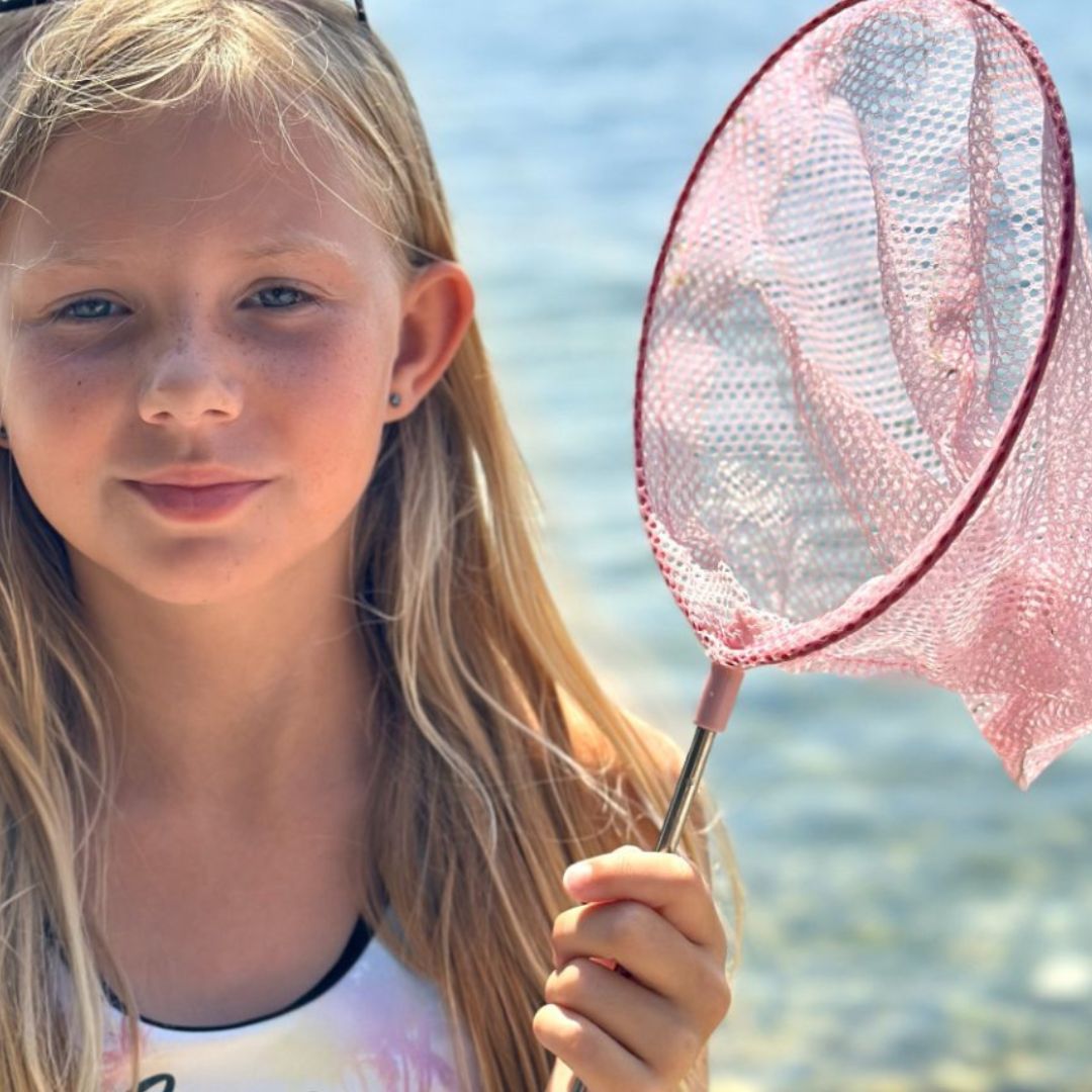 Pige ved strand holder rosa fiskenet på teleskopstang, fås hos Nordic Simply