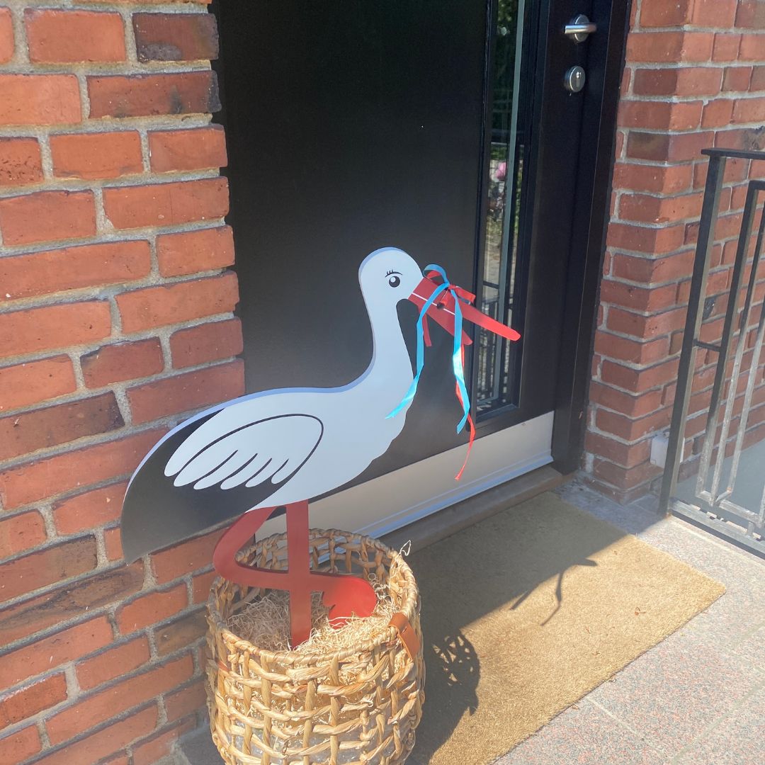 fødselsstork og barselsstork 80 cm fra Magni står i kurv foran sort hoveddør klar til at fejre en lille ny, set hos Nordic Simply