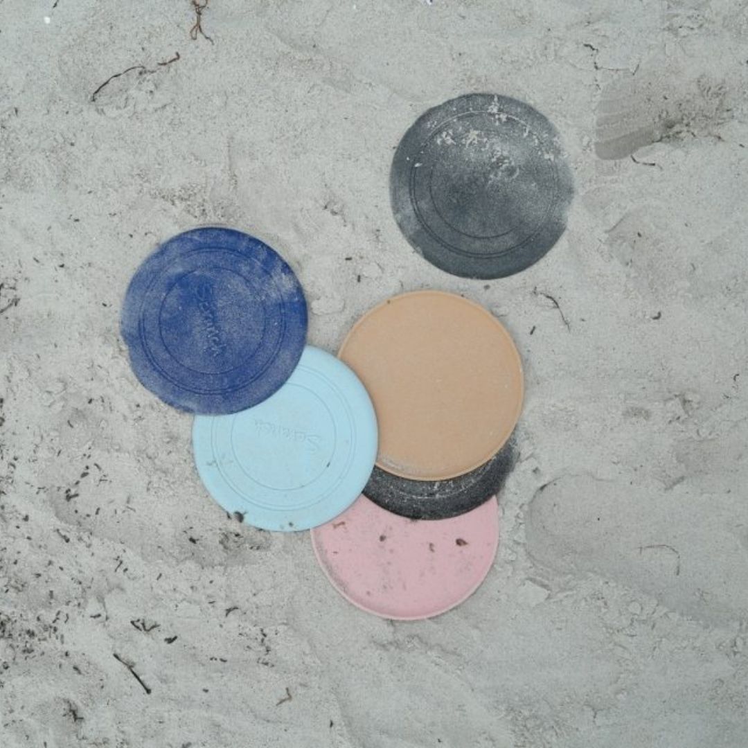 Frisbees i silikone fra Scrunch ligger i sand, set oppefra, rosa frisbee fås hos Nordic Simply