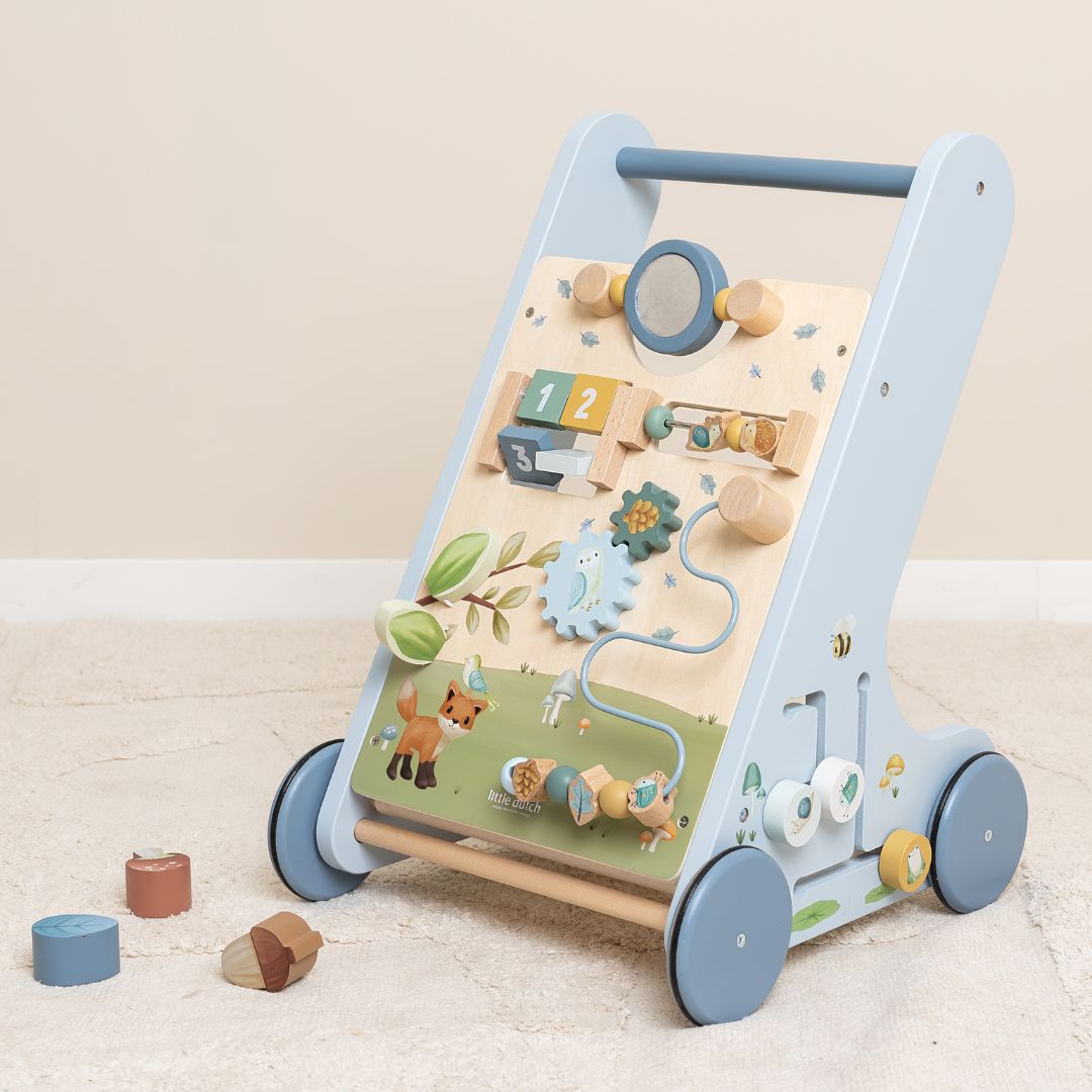 Blå aktivitets gåvogn i træ, Forest Friends, fra Little Dutch, med 8 spændende aktiviteter at opdage og udforske, står på lyst tæppe i stue.
