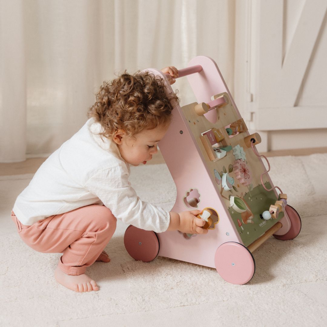 Barn leger med rosa gåvogn i træ med 8 aktiviteter fra Little Dutch, designet til at støtte motorisk udvikling for børn fra 1 år.