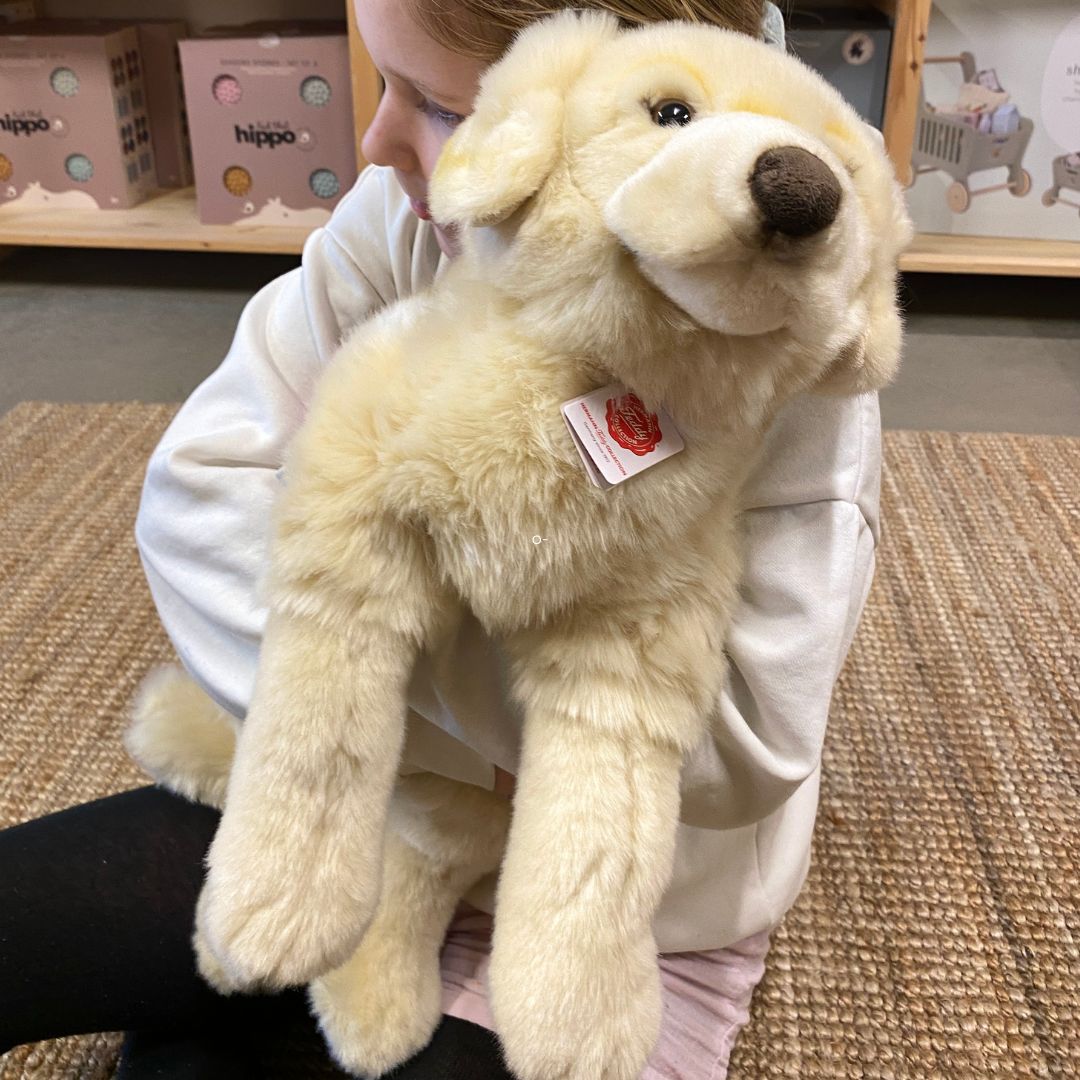 barn sidder med stor lys Golden Retriever bamse, på lyst gulvtæppe hos danske Nordic Simply - en blød og krammevenlig bamse til leg